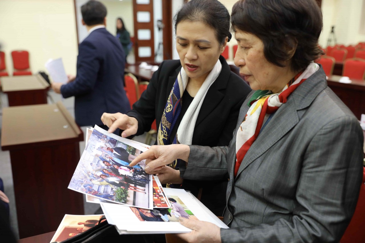 Ambassador Dinh Thi Minh Huyen (first, from right) and Ambassador Nguyen Phuong Nga review photos of a group of Vietnamese Agent Orange victims taken with Ms. Merle Ratner in 2008 in the US. (Photo: Dinh Hoa)