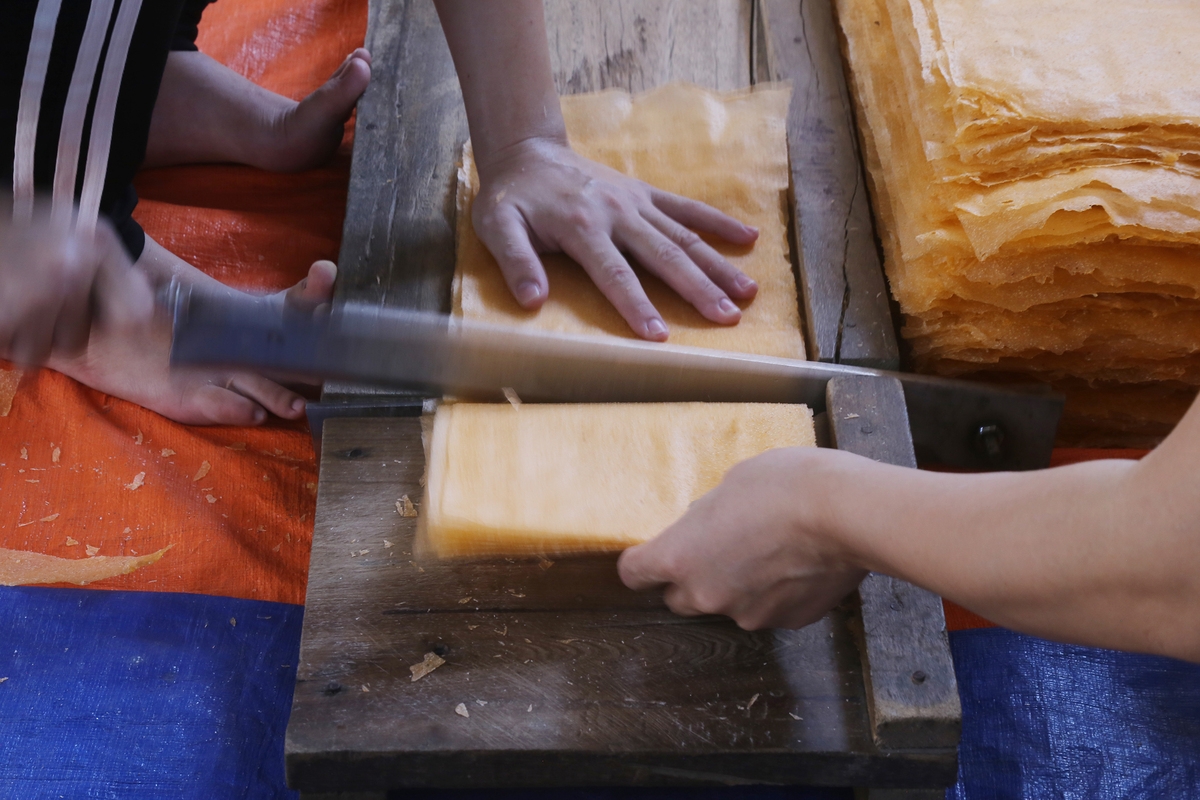 Rice papers are placed into stacks of 20 pieces and cut into squares.